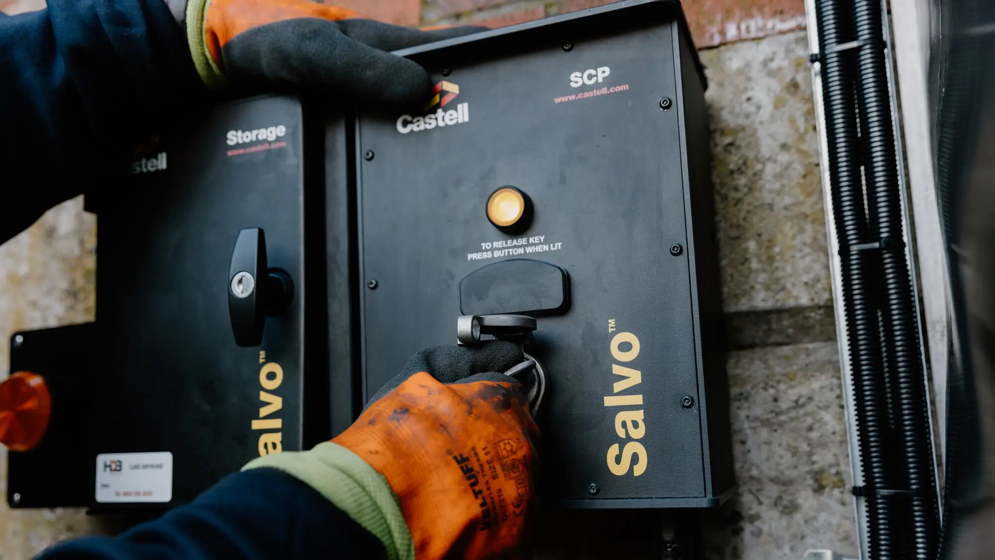 Worker in safety gloves operating a Castell Salvo SCP trapped-key interlock unit mounted on a loading bay wall, pressing the illuminated button to release the key.