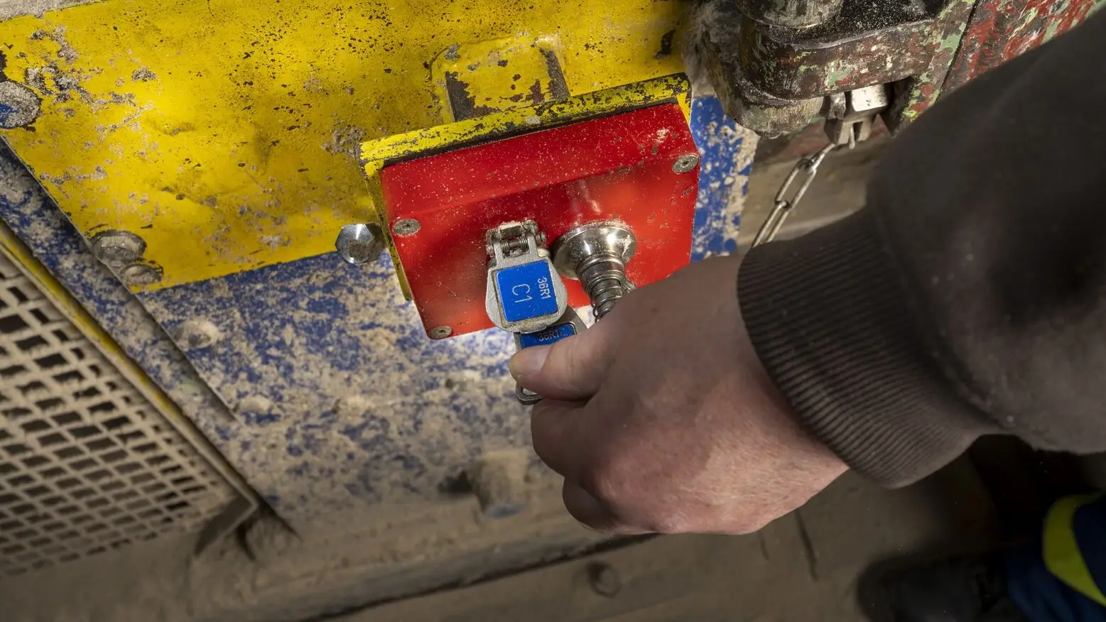 Worker turning a key in a red STi access interlock mounted on dusty industrial machinery