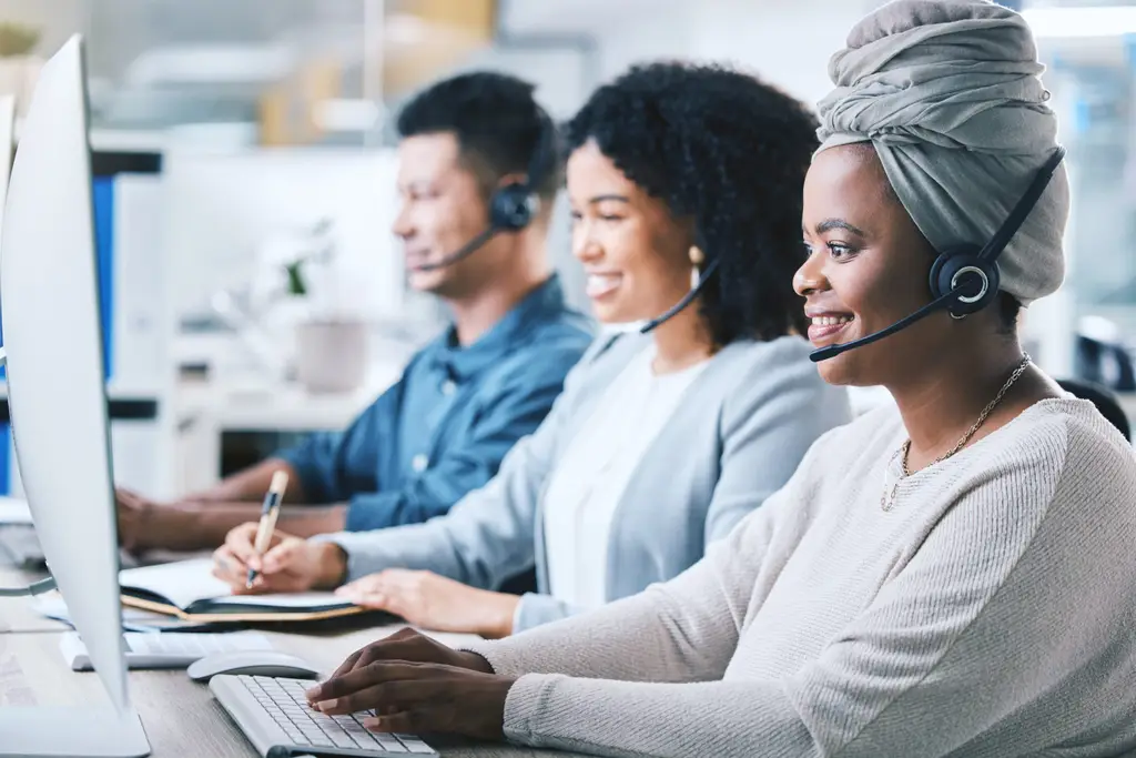 Customer service, call center and a team at computer with a headset for contact us website. Black woman and employees as crm, telemarketing or sales support agent with headphones, smile and desktop.