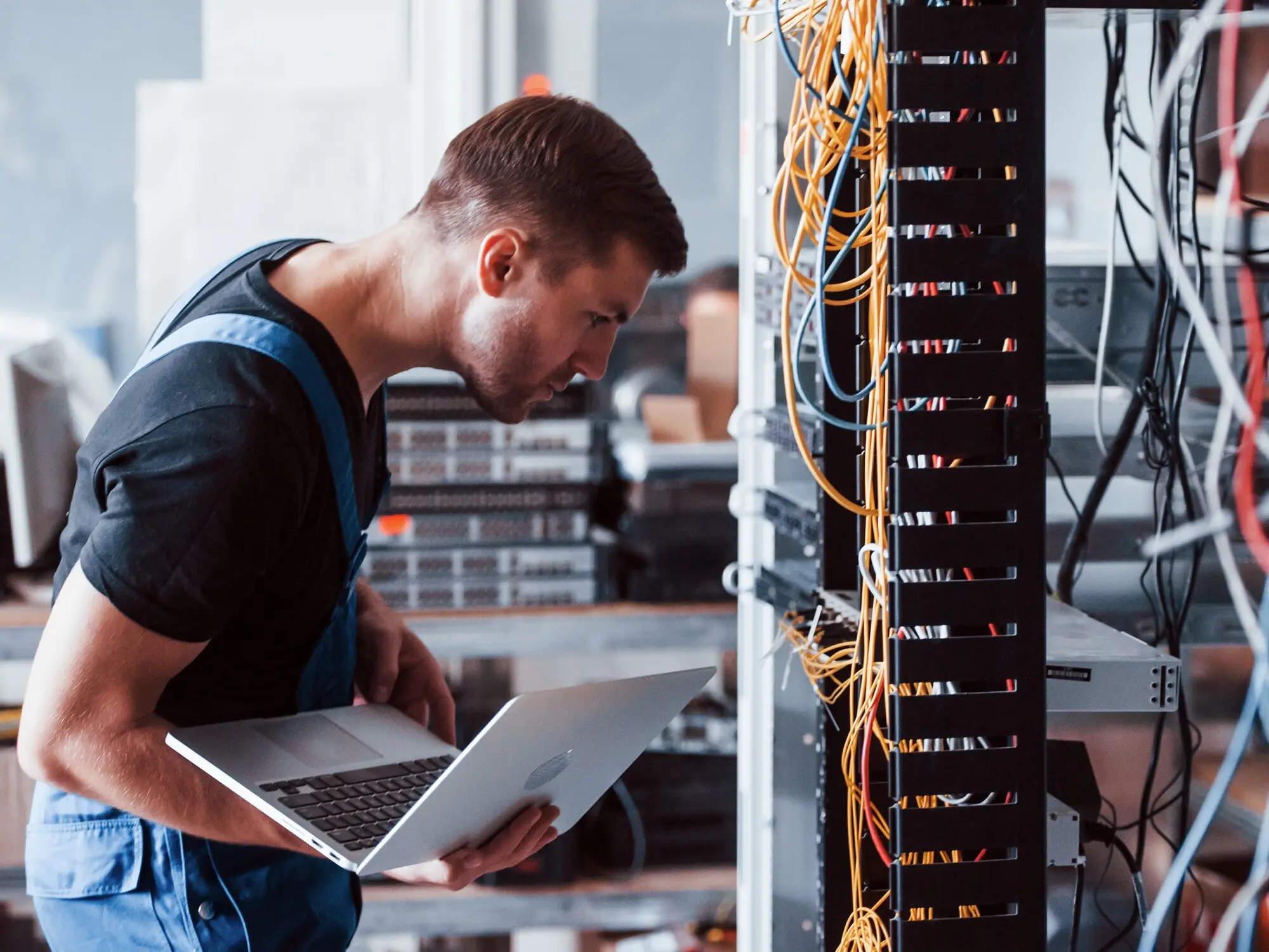 Worker holding a laptop and inspecting cables and equipment in a controlled area of hazard