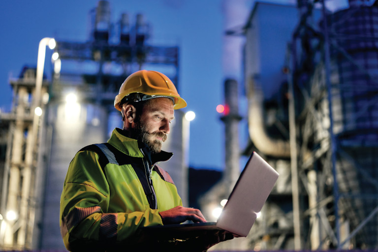 Young engineer wearing a helmet and using a laptop during his night shift. Engineering concept.